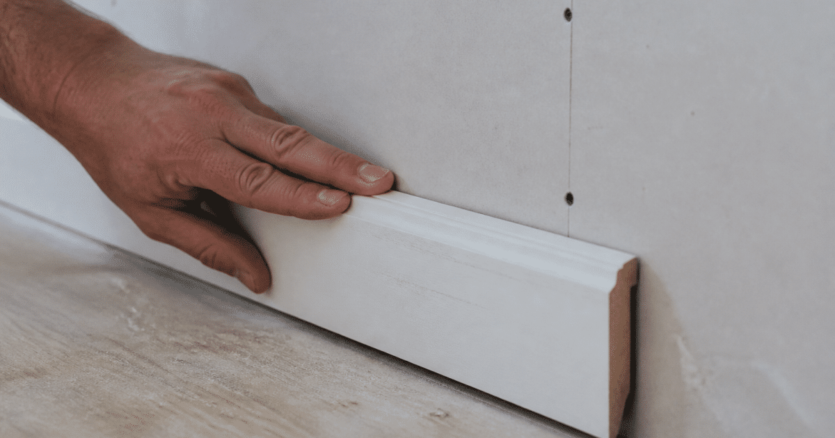 Main vissant plinthe blanche contre mur placo vertical