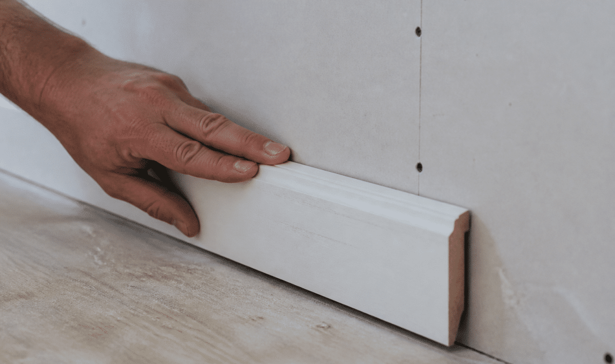 Main vissant plinthe blanche contre mur placo vertical