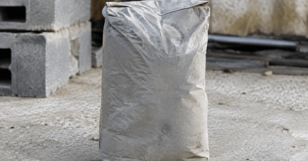 Sac de ciment gris posé debout sur sol beton