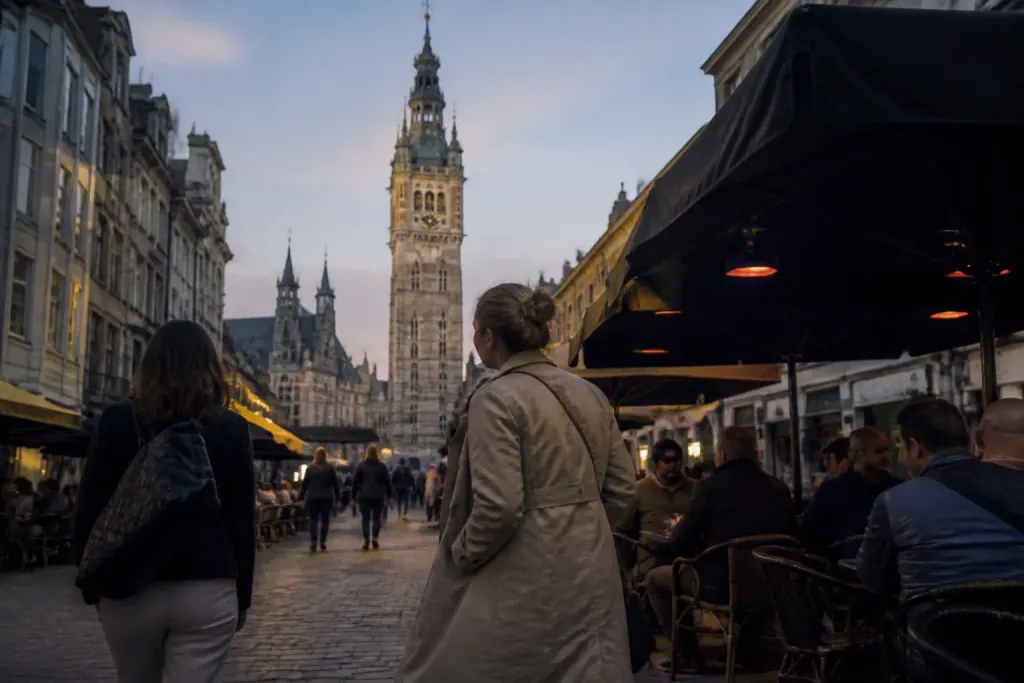 Passants devant des terrasses pres du beffroi au crepuscule