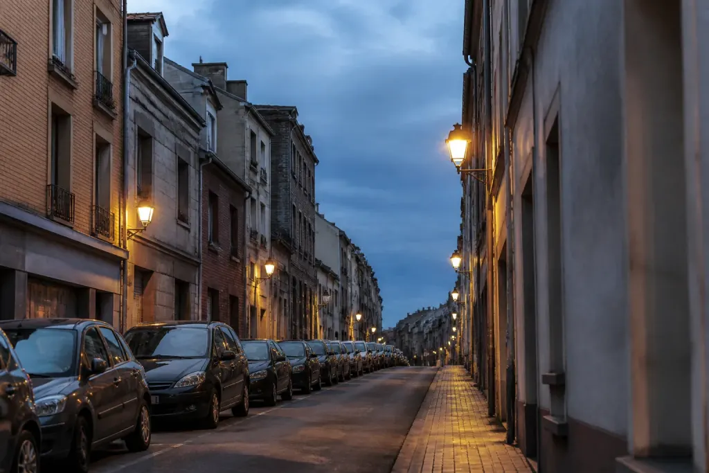 Rue commercante au crepuscule, lampadaires allumes et voitures garees
